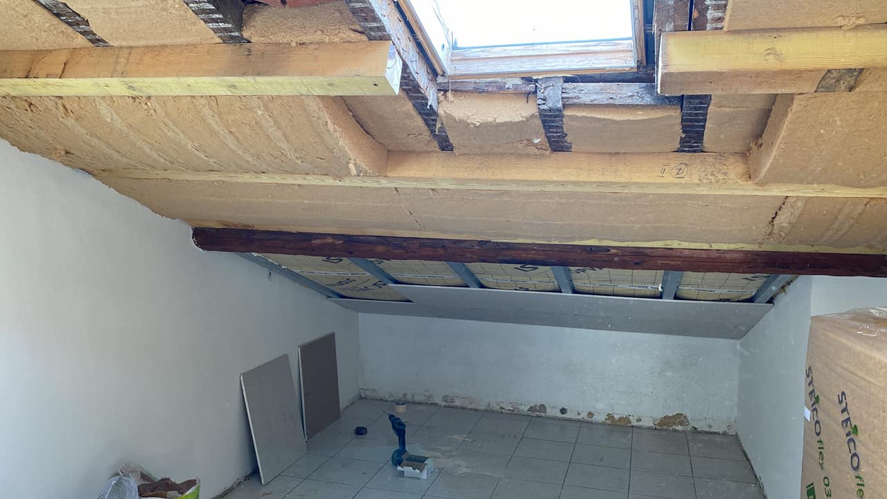 Chantier d’isolation thermique avec pose de panneaux isolants sous toiture inclinée, autour d’une fenêtre de toit.